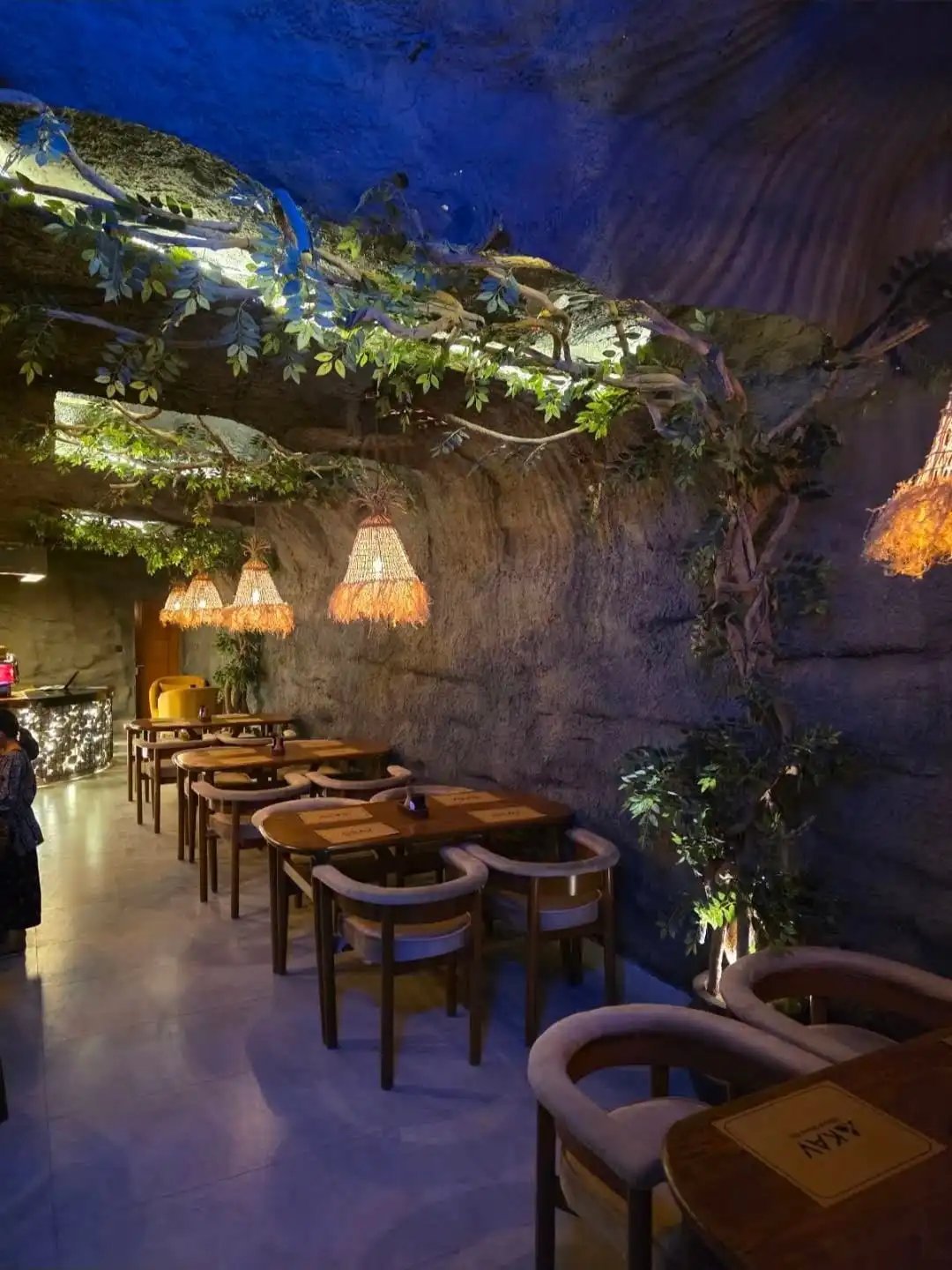 KAV dining room with wooden tables, rattan pendant lights, hanging vines and atmospheric blue lighting on textured walls